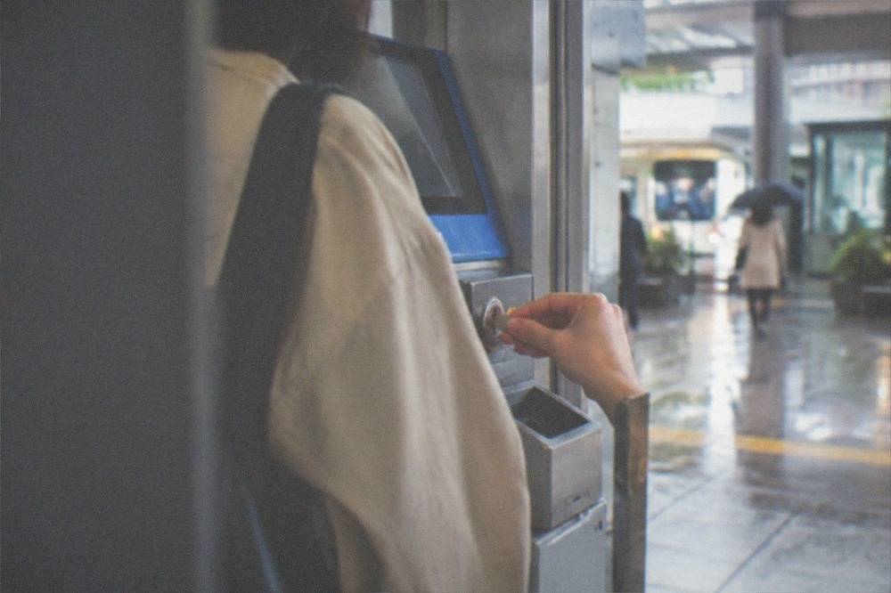 A hand inserting coins into a train station fare top-up machine