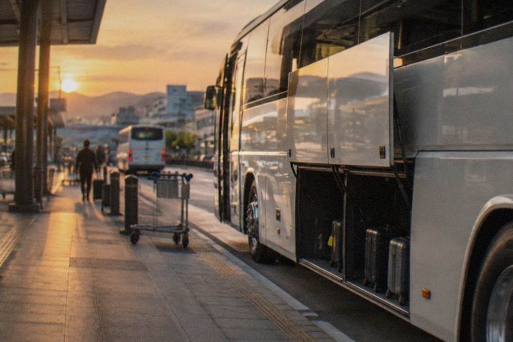 A limousine airport bus parked at a terminal curb beside luggage-loading bays