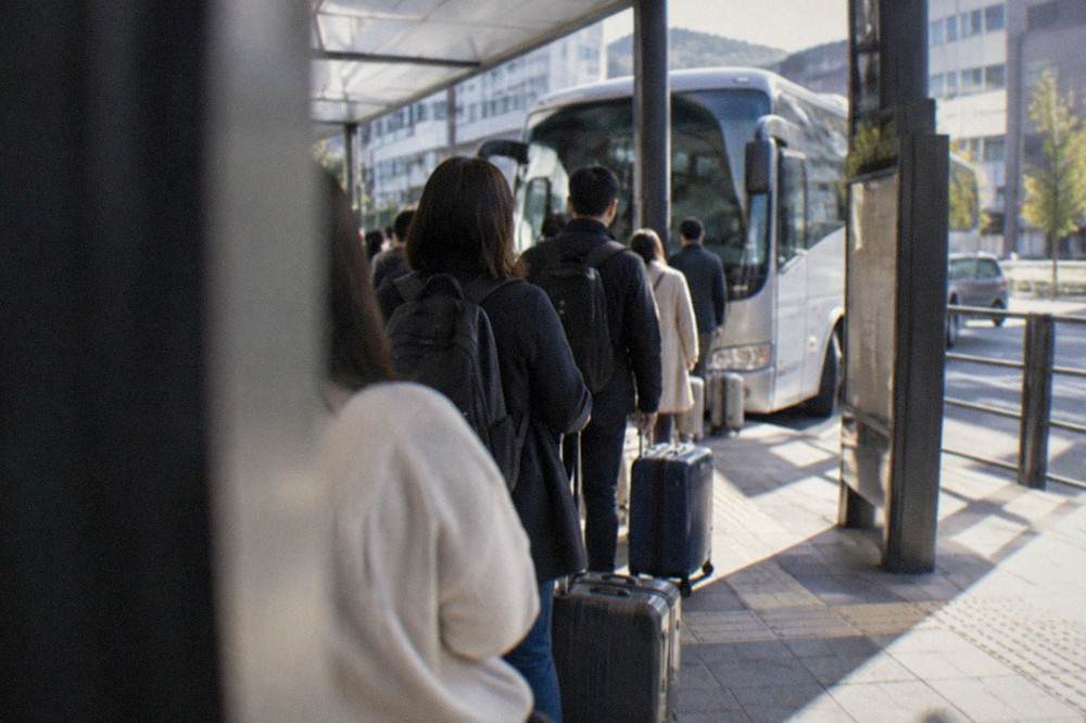 Travellers with suitcases waiting in a sheltered line at an airport bus stop in Japan