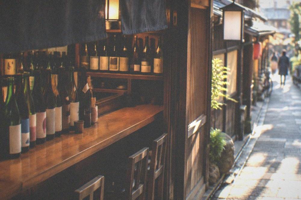 Rows of sake bottles lined up behind a wooden izakaya bar counter