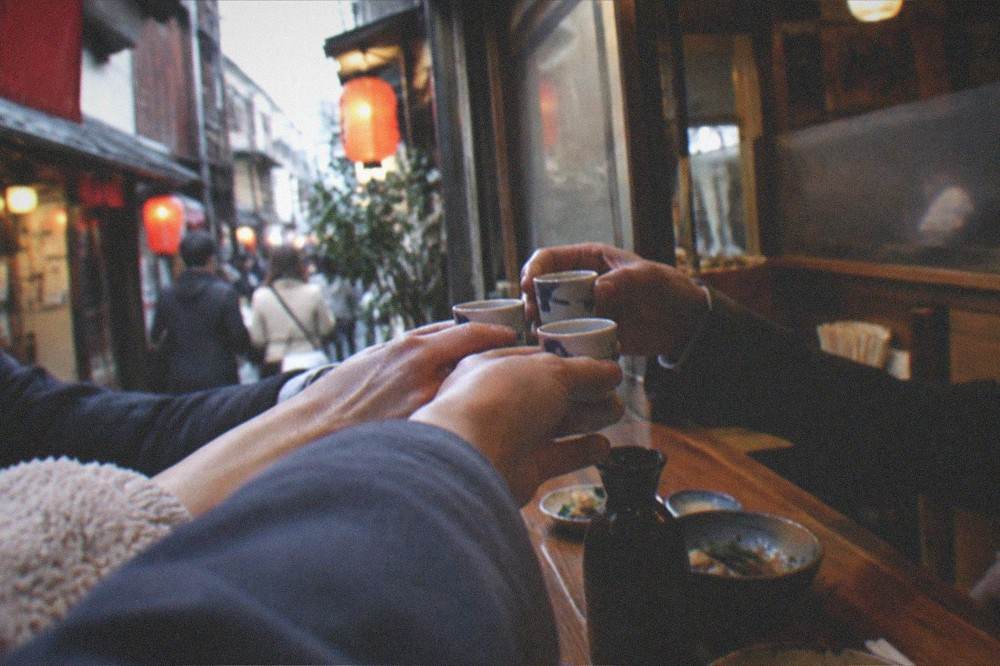A small group raising glasses of sake at a crowded izakaya counter