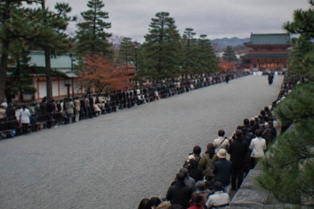 Rows of spectators lining a wide gravel path waiting for a historical procession in Kyoto