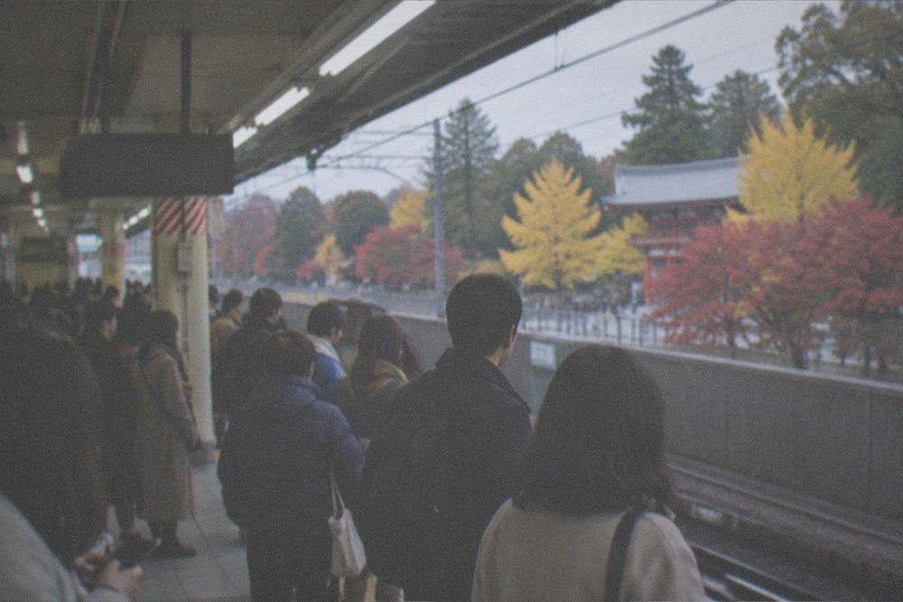 A crowded Kyoto subway platform with morning commuters and visitors in autumn clothing