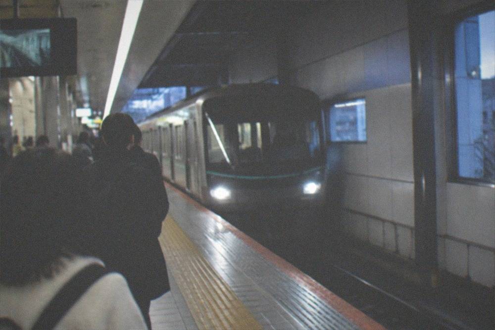 A Kyoto subway platform with a train arriving and travellers looking at the route map