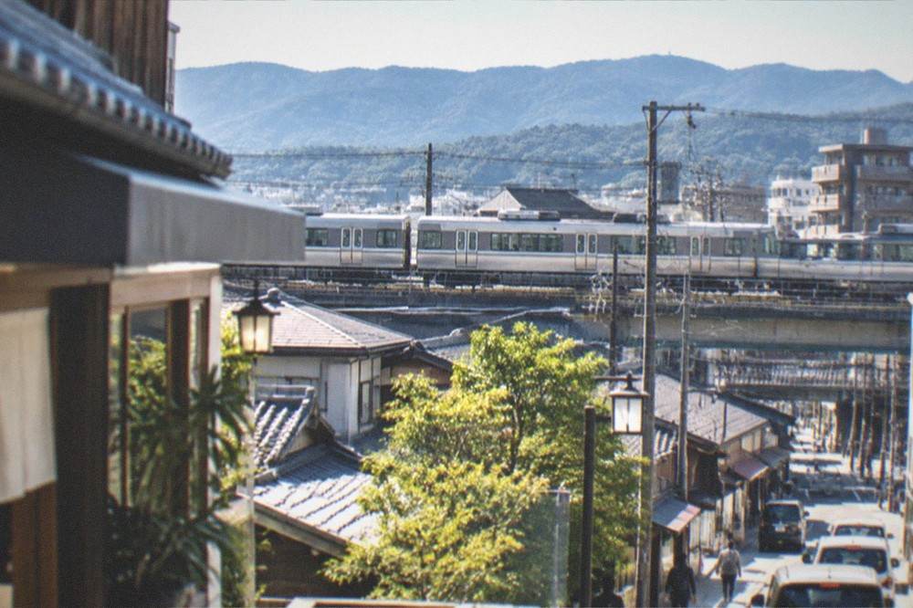 A commuter train passing the rooftops and hills on the edge of Kyoto