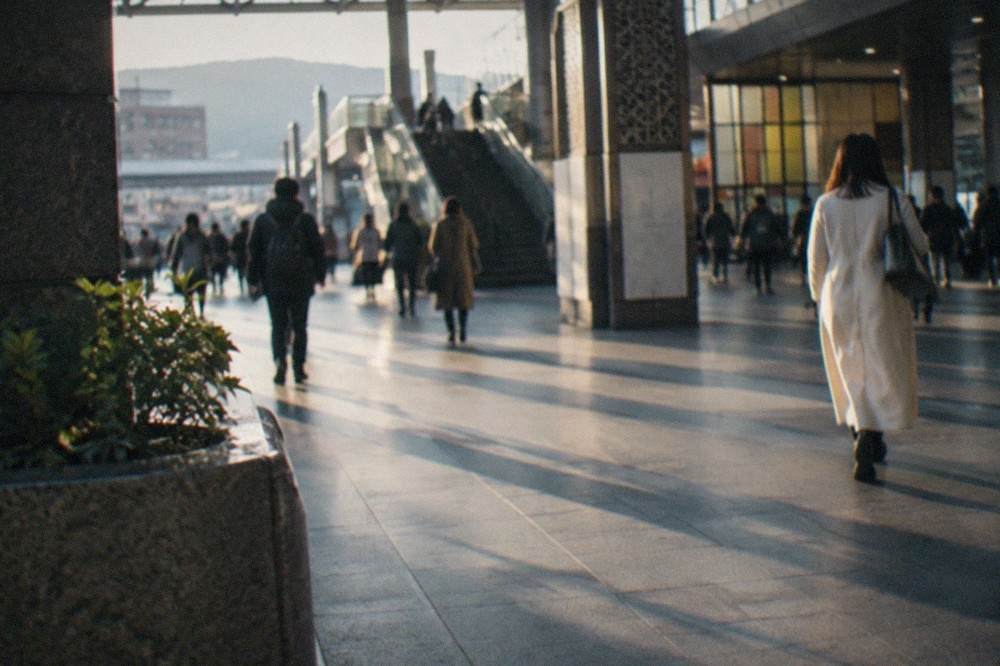 A wide station concourse with departure boards and travellers with rolling suitcases