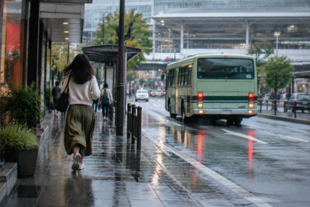 A city bus pulling away from a stop outside a large rail station