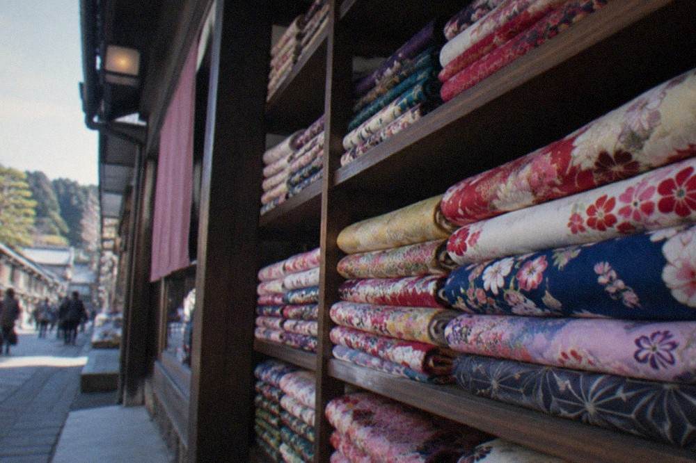 Rows of folded kimono in bright patterns stacked on shelves inside a rental shop