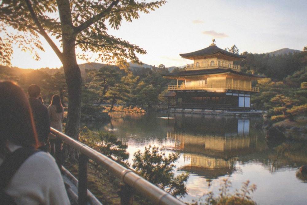 A golden pavilion reflected in a pond seen from a level viewing area