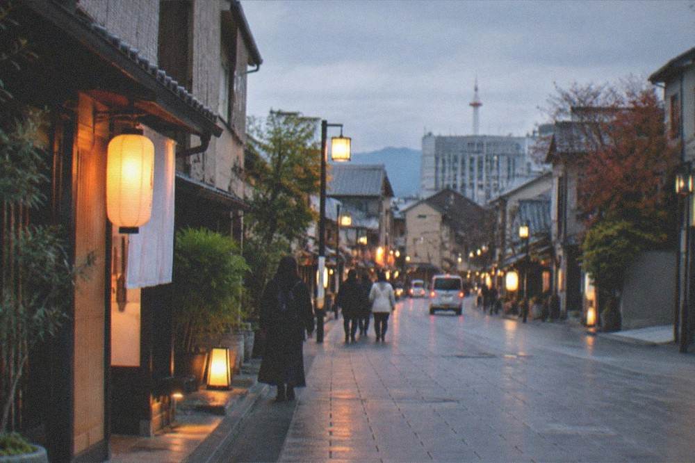 A wide lantern-lit street in Kyoto at dusk with level paving and no crowds