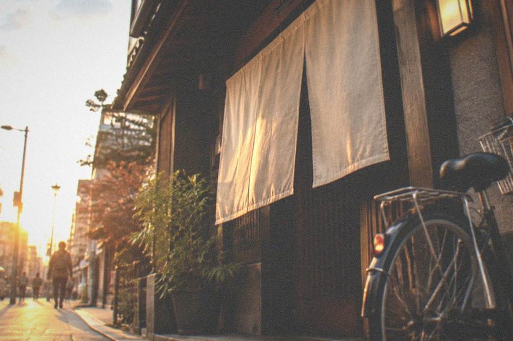 A guesthouse entrance in Kyoto with noren curtains and a bicycle parked outside