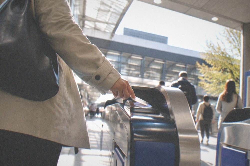 A commuter tapping a smart card on a ticket gate reader at a subway station