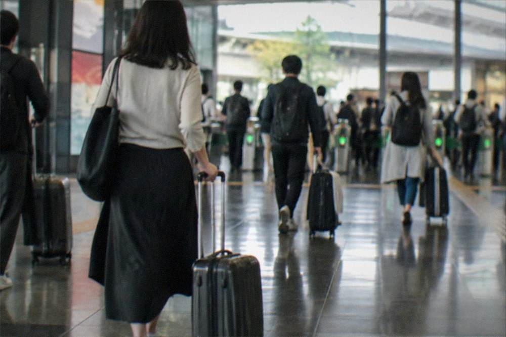 Travellers with suitcases walking through a busy station concourse toward ticket gates