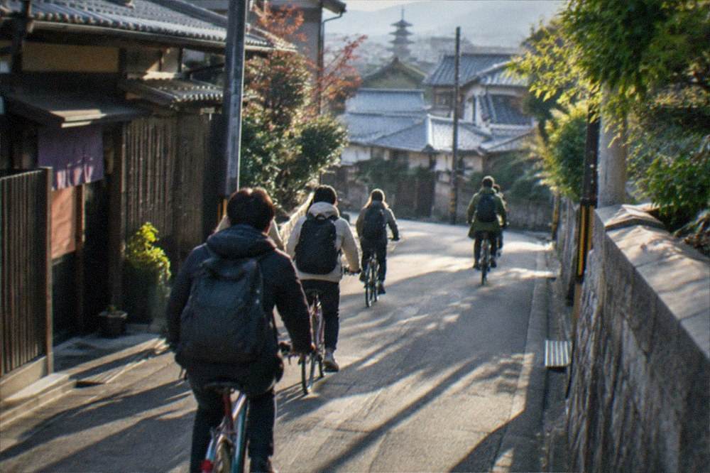 A small group of cyclists following a guide along a narrow residential street in northern Kyoto