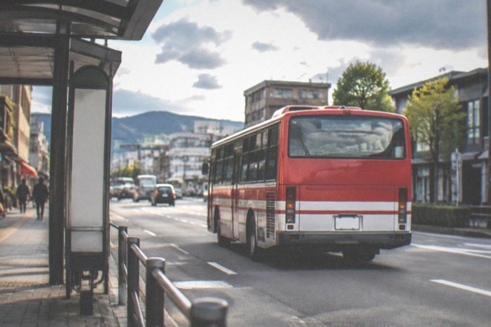 A red and white limited express bus pulling away from a Kyoto bus stop