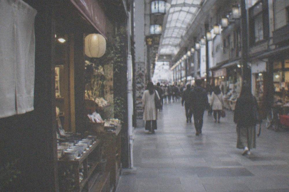A covered shopping arcade in downtown Kyoto with small shopfronts and pedestrians