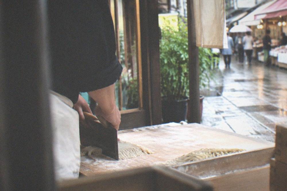 Fresh ramen noodles being cut on a floured wooden board during a class in Kyoto