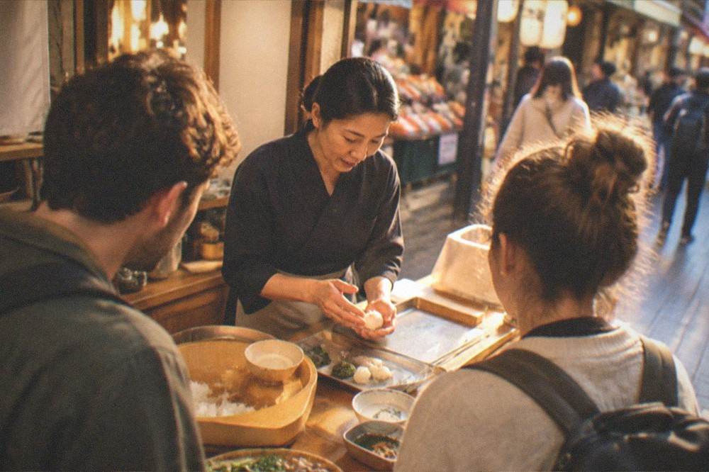 A Kyoto cooking instructor explaining a recipe to two travellers at a kitchen counter