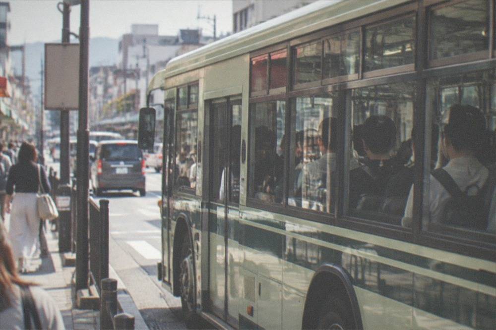 A city bus packed with passengers at a stop on a busy street in central Kyoto