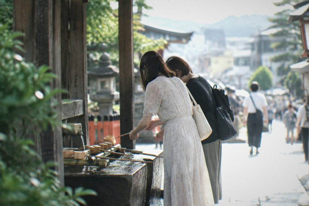 Visitors washing their hands with wooden ladles at a stone water pavilion outside a Kyoto shrine
