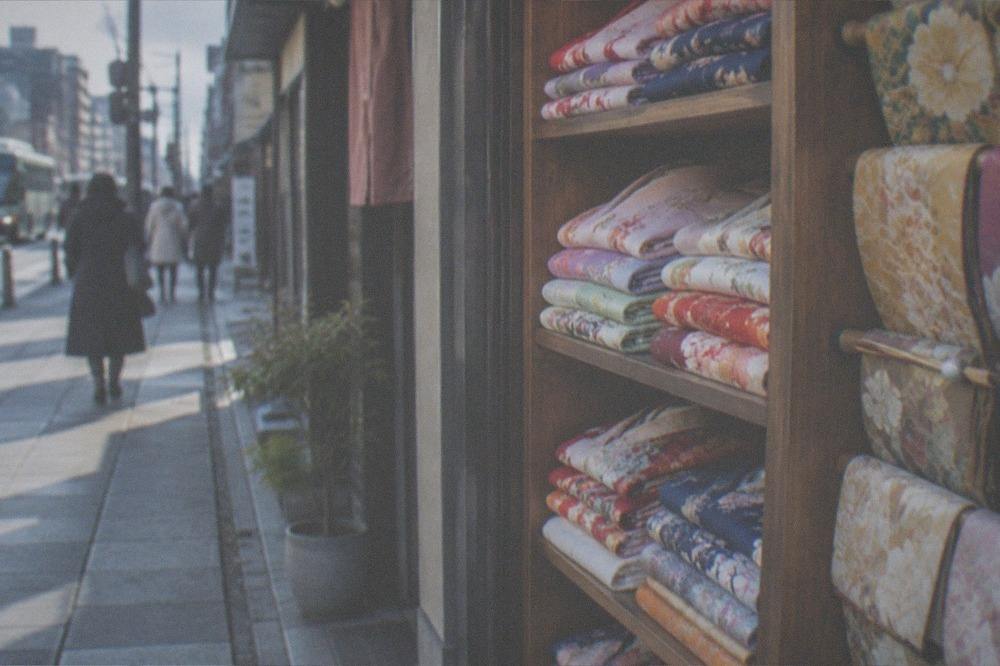 A row of colourful folded kimono and obi sashes on wooden shelves in a Kyoto rental shop