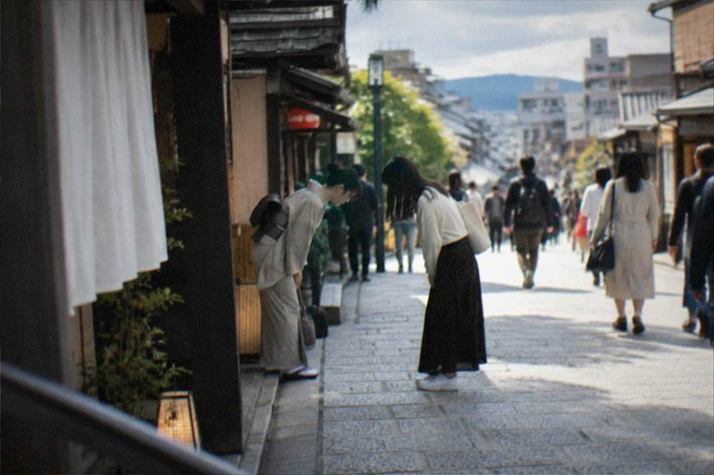 Two people bowing slightly toward each other in greeting on a Kyoto shopping street