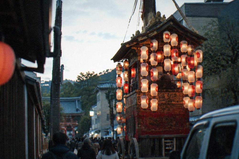 A tall wooden festival float crowded with lanterns on a Kyoto street at dusk