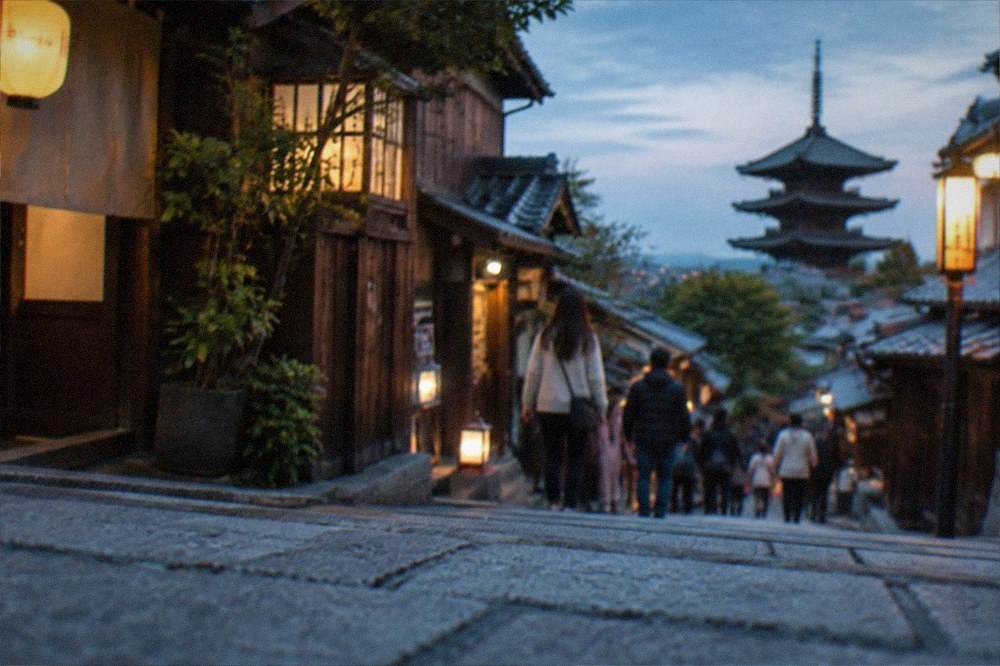 Visitors walking a stone paved slope among traditional wooden buildings in Kyoto