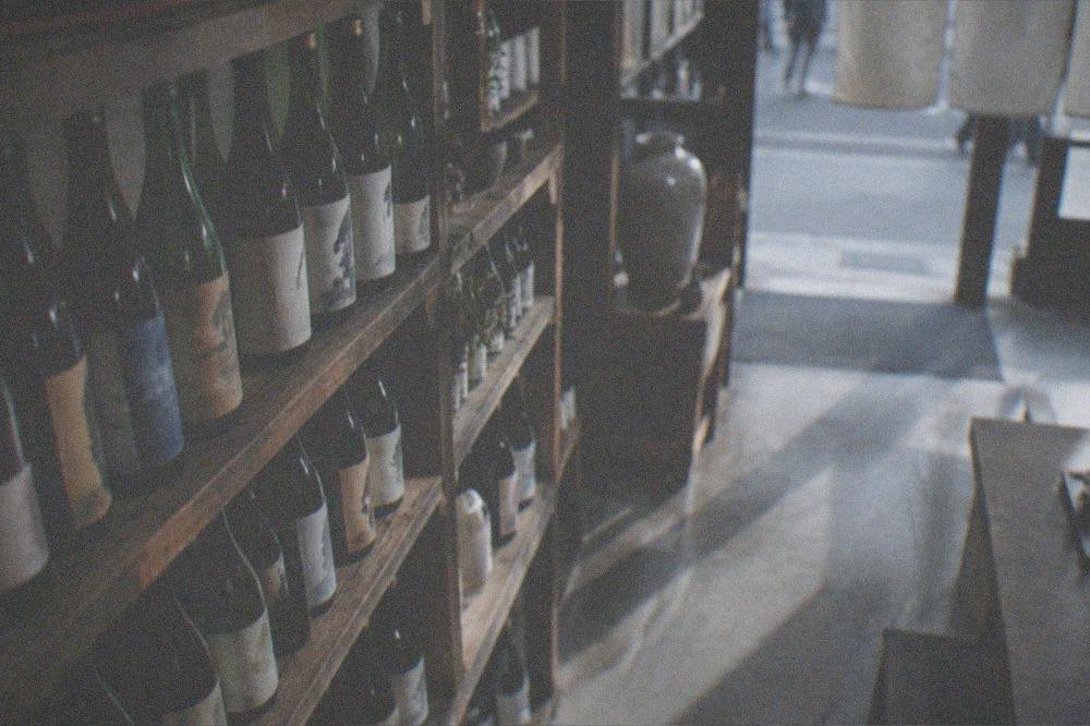 Sake bottles lined up on wooden shelves in a traditional brewery tasting room