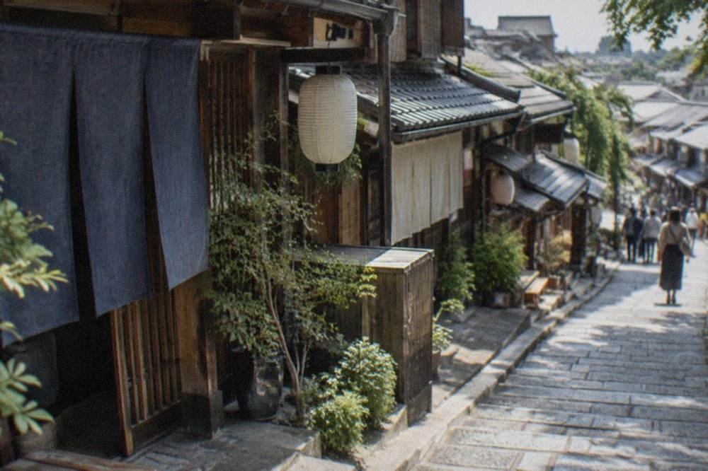 A narrow stone lane in Kyoto lined with traditional wooden machiya houses and hanging noren curtains