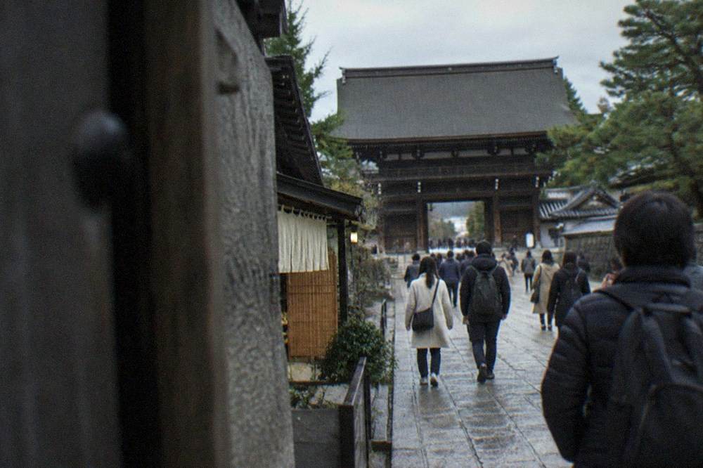 Visitors walking along a stone path toward a large wooden temple gate in Kyoto