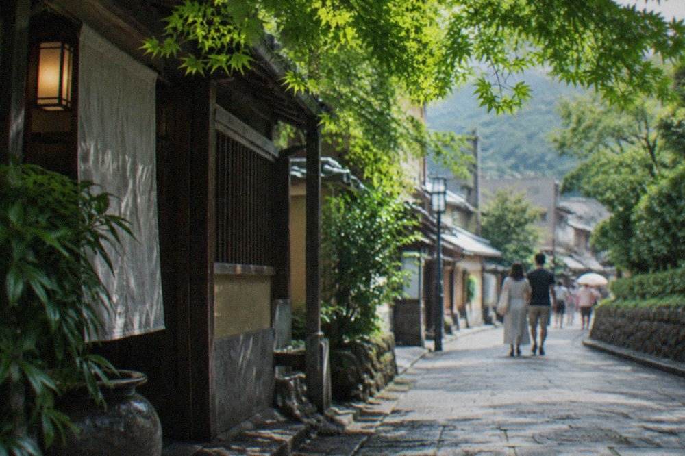 A shaded Kyoto street in summer with green maple leaves filtering bright sunlight onto a stone lane