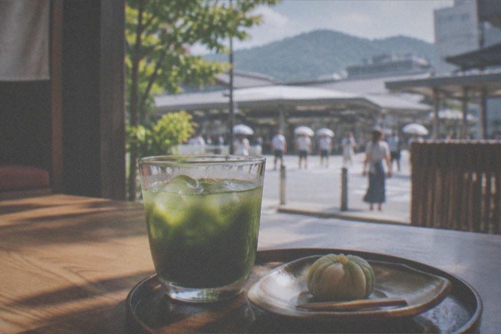 A cold glass of matcha tea and a wagashi sweet on a wooden table in a shaded room