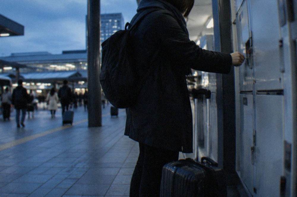 A traveller inserting a coin into a station locker with a suitcase at their feet
