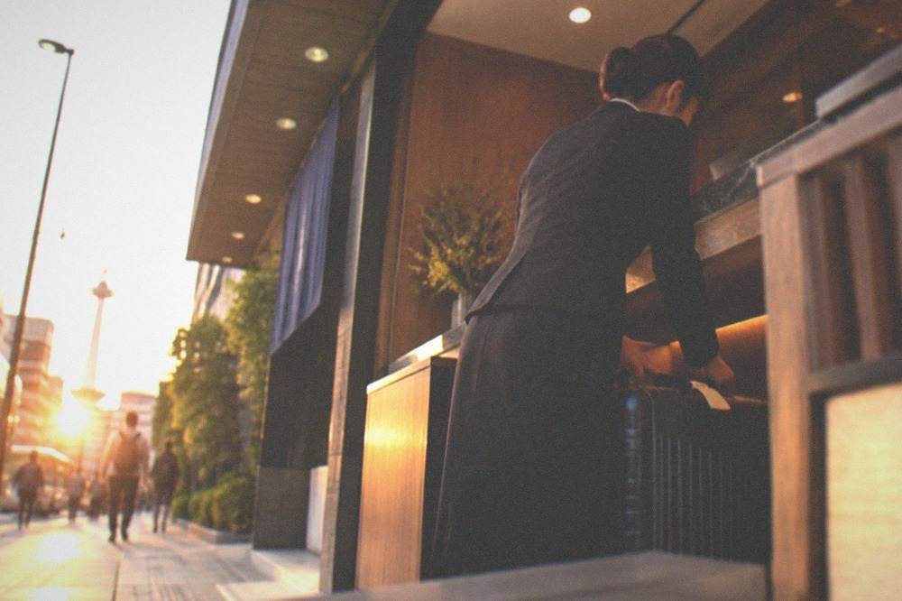 A hotel front desk clerk storing a tagged suitcase behind the counter