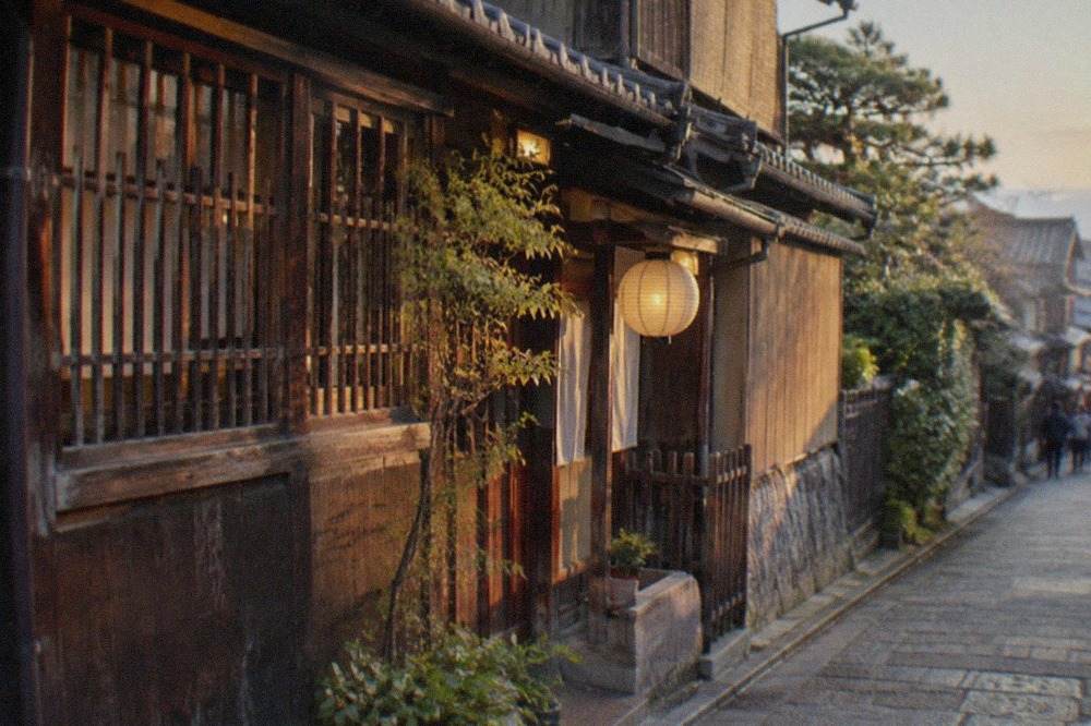 A narrow wooden Kyoto townhouse facade with lattice windows and a tiled roof above a quiet stone lane