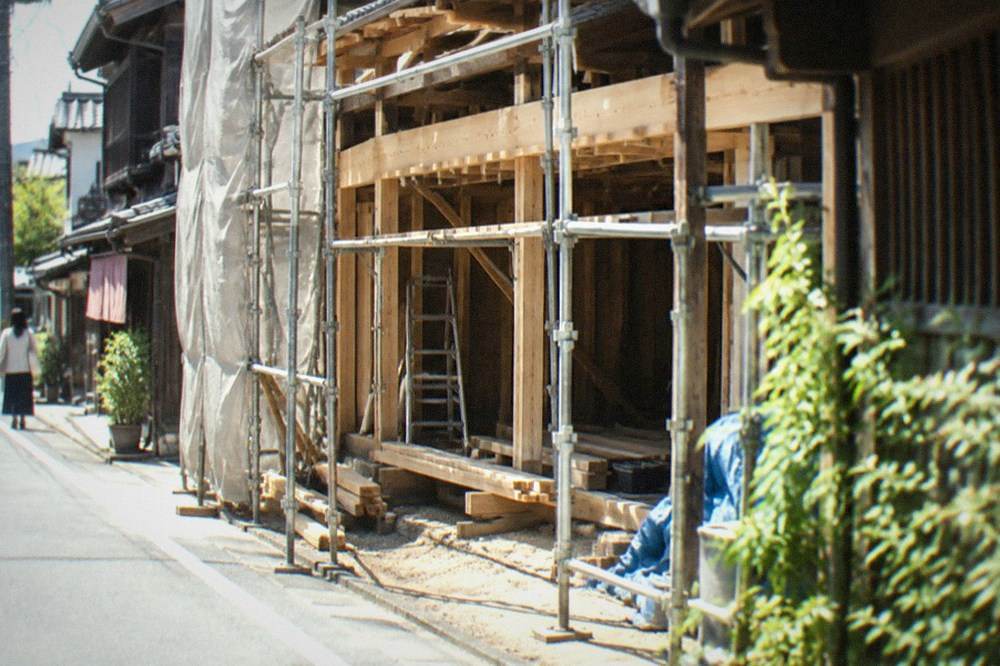 An old wooden townhouse being restored, with scaffolding and fresh timber beams over a dusty workshop floor