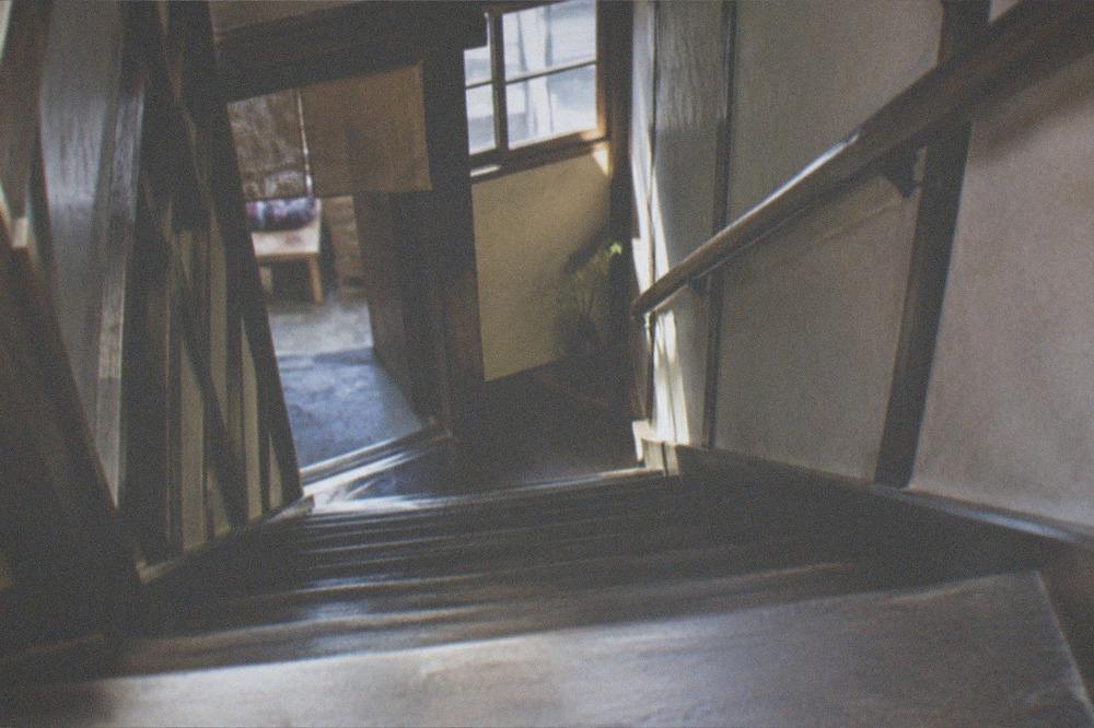 A steep narrow wooden staircase inside a traditional townhouse lit by a small window