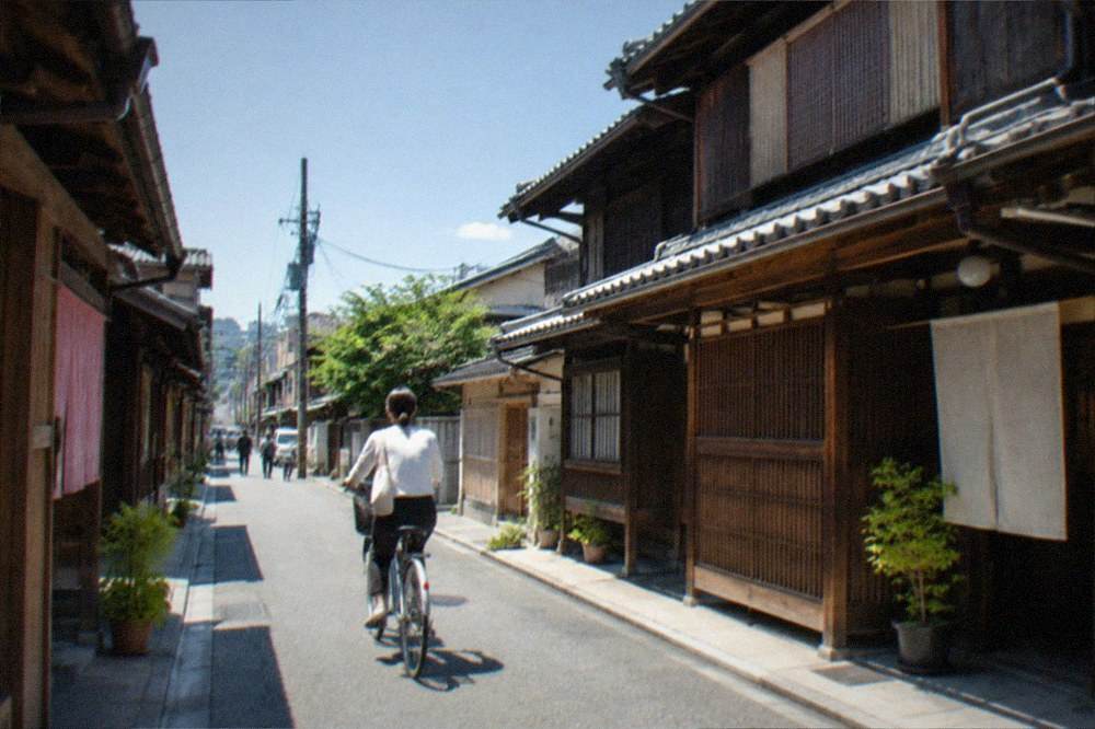 A cyclist on a narrow Kyoto street lined with traditional wooden houses in morning light