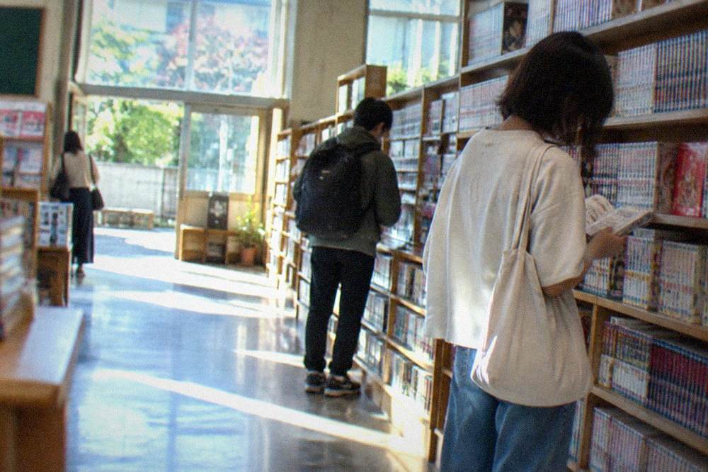 Visitors reading manga volumes on shelves inside a converted school building