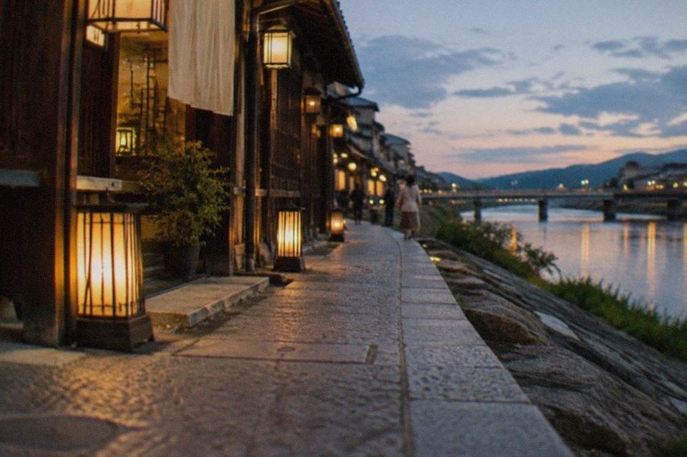 Lanterns glowing along a narrow stone alley beside the Kamo River in Kyoto at night