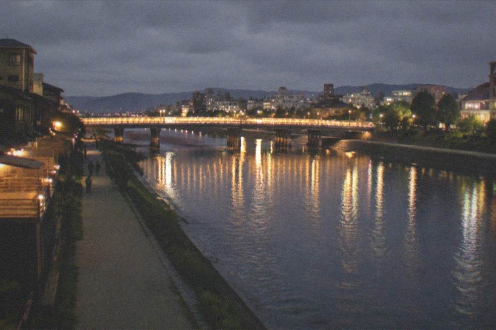 The Kamo River in Kyoto at night with the lit bridges and city skyline reflected in the water