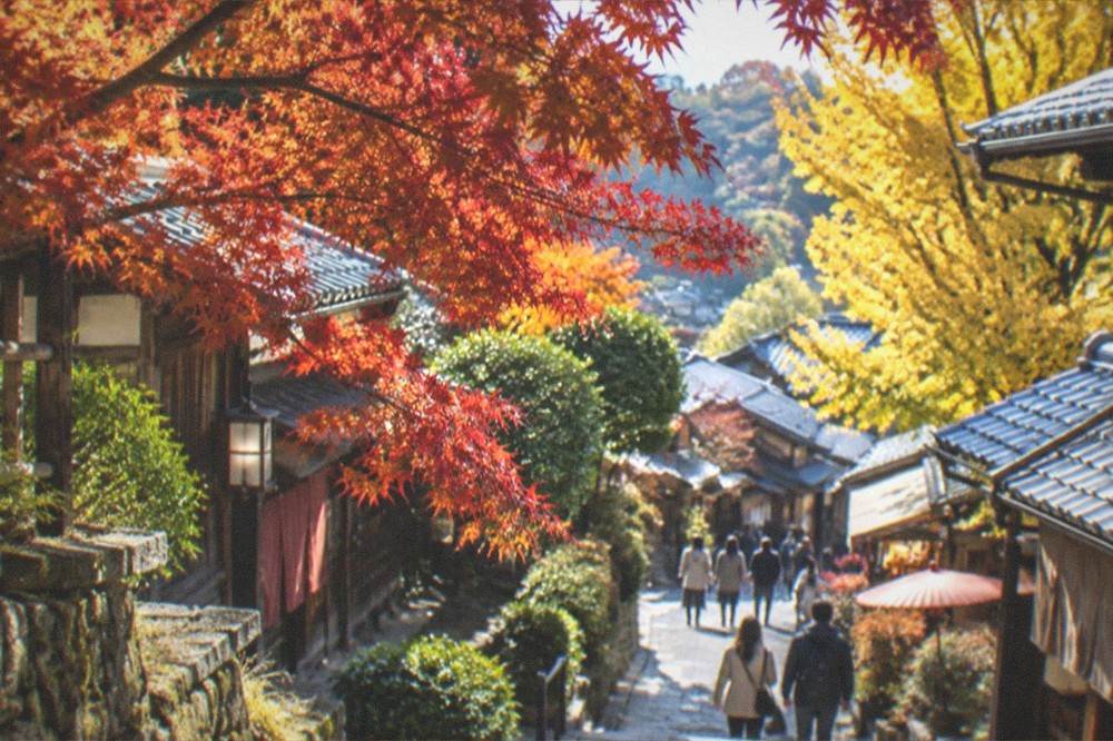Red and orange maple branches overhanging a stone temple path in late autumn light