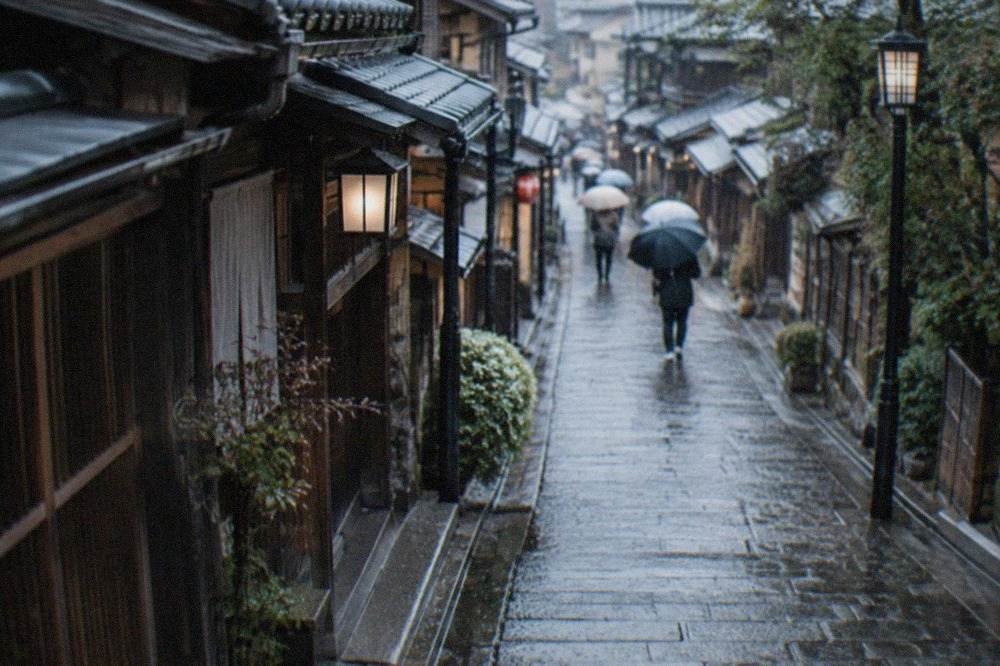 Rain falling on a stone lane lined with traditional wooden machiya townhouses in Kyoto