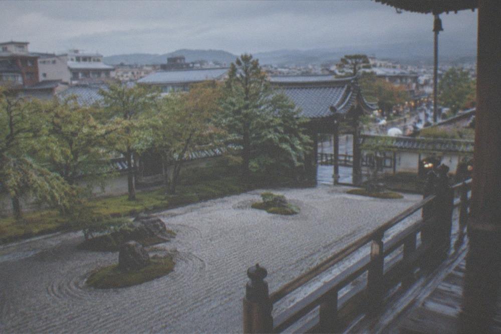 A raked gravel zen garden glistening with rain viewed from a wooden temple veranda