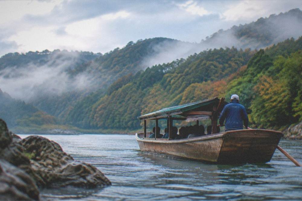 A wooden river boat on the Hozugawa with mist over forested hills in Kyoto