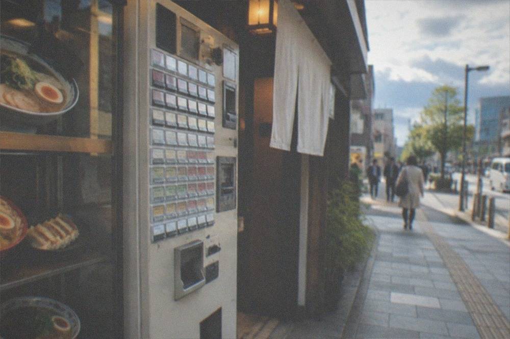 A ramen shop ticket machine with plastic food models in a glass case