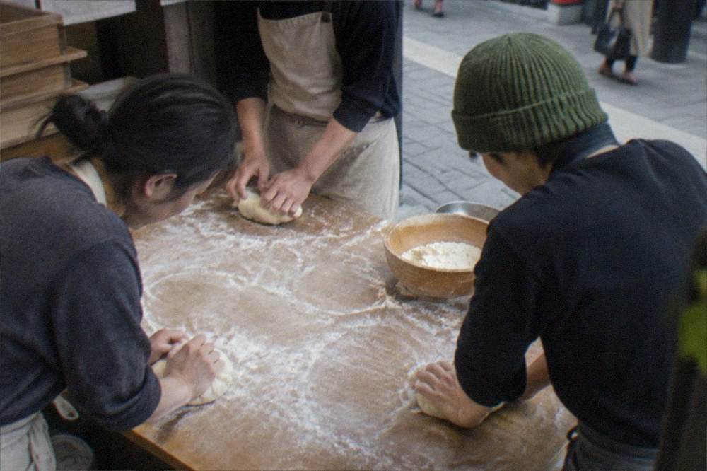 A small group kneading ramen noodle dough on a floured wooden table