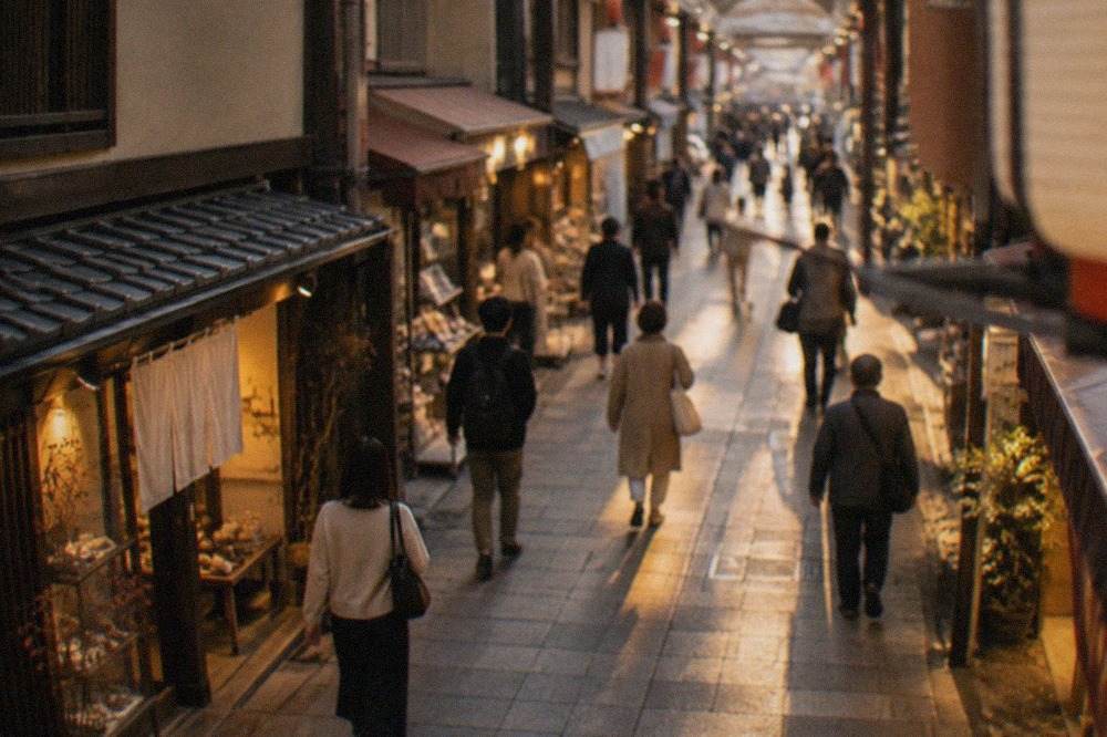 A covered shopping arcade in Kyoto with small lit shopfronts on both sides and pedestrians walking through