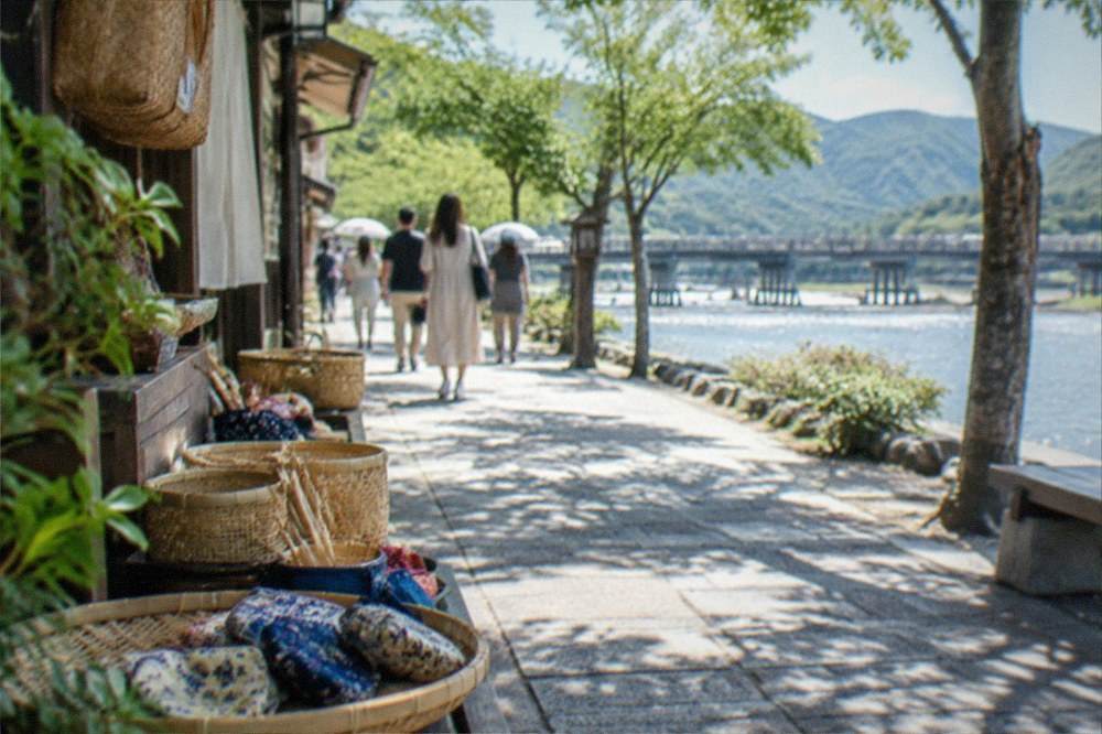 A riverside street in Arashiyama with small craft shops and visitors strolling under trees